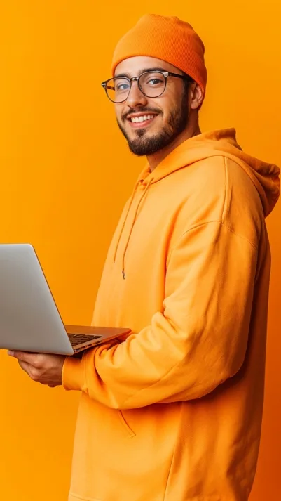 Rapaz sorridente de óculos e moletom laranja segurando um notebook